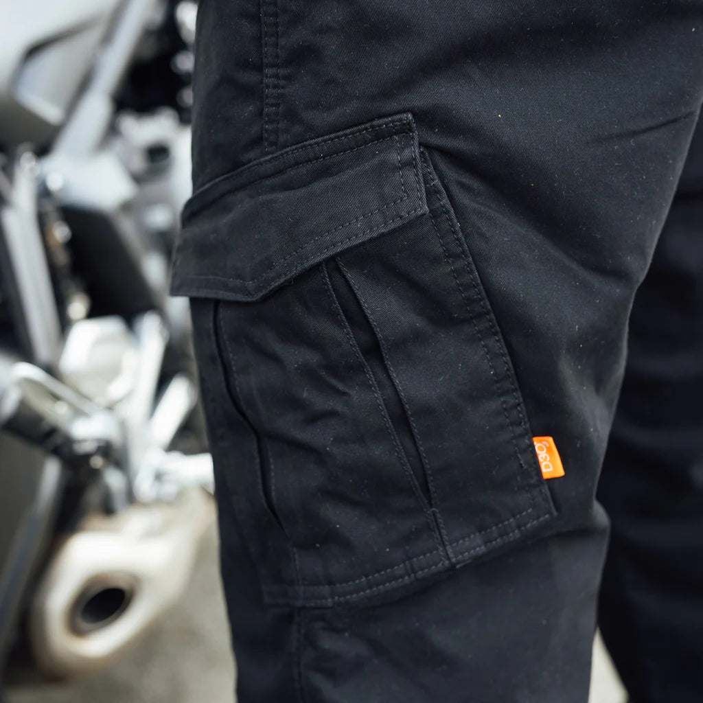 close up of Person wearing black Merlin Remy CE UKCA AA rated protective motorcycle trousers with an orange D30 armour tag on a blurred motorcycle background
